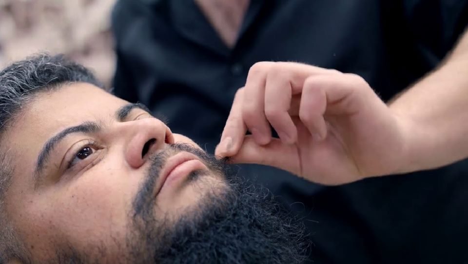 Light-skinned man with black hair and a large black beard being touched by a light-skinned hand - Metropolis